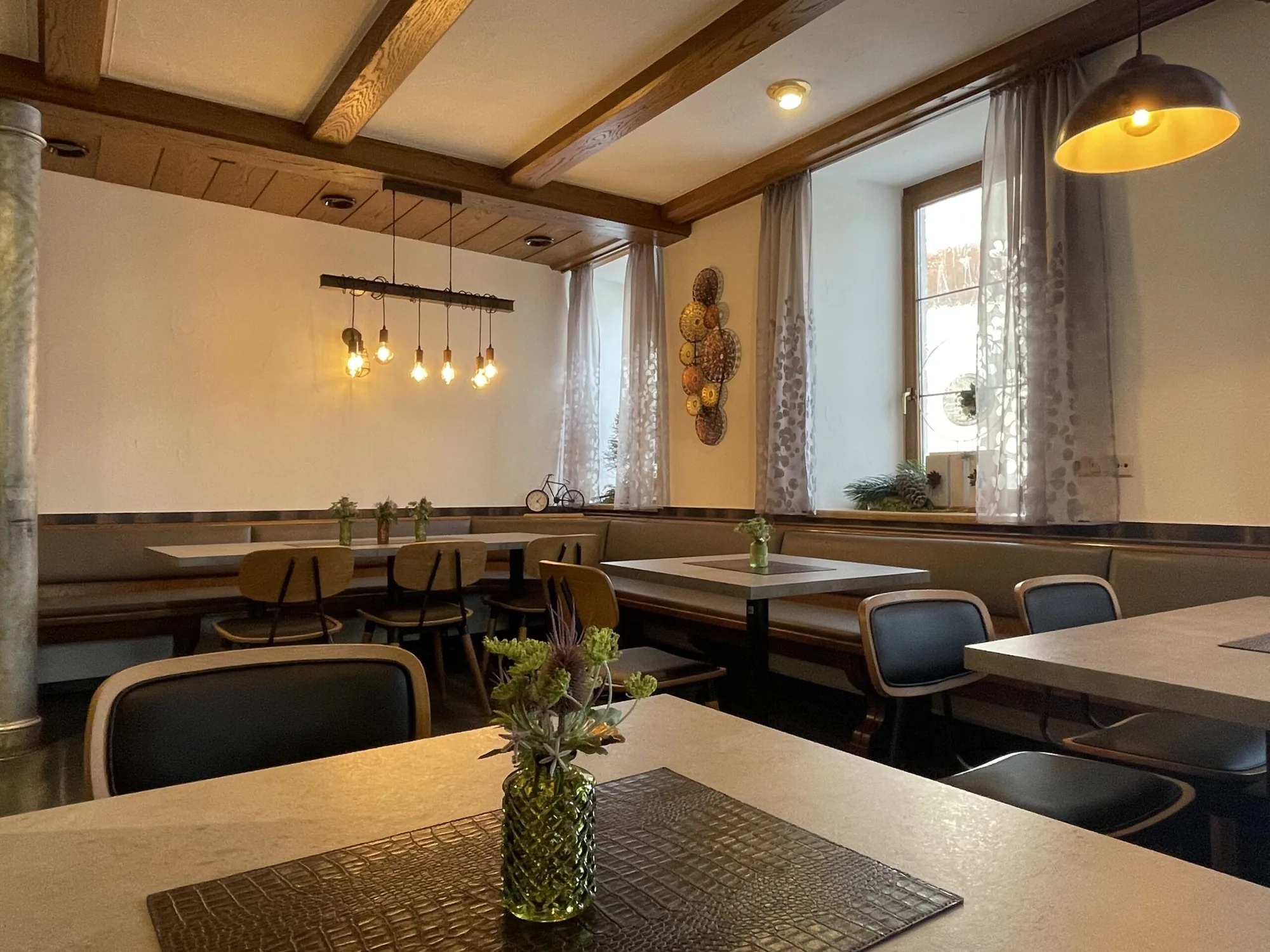 Gaststube mit warmem Licht, Holzbalken und gedeckten Tischen